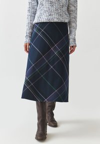 Jupe à carreaux bleu marine avec un design mi-long avec des lignes vertes, roses et bleues. Associée à des bottes marron jusqu'au genou et un pull texturé.