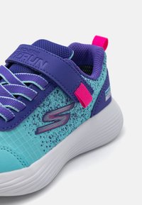 Sportschuhe mit einem Obermaterial aus blauer und türkisfarbener Mesh, lila Akzenten und einer pinken Fersenschlaufe. Mit einem Klettverschlussriemen und einer strukturierten Sohle.