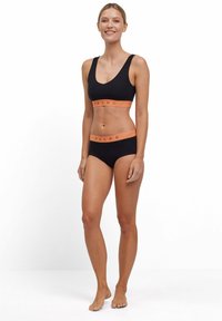 Zwart sportbh en slipset met een oranje elastische band met het label "FALKE"; soepel materiaal, aansluitend ontwerp, minimalistische stijl.
