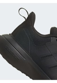 Svart sportskor med meshinlägg, texturerade accenter och en tjock sula. Har en dragflik och präglad branding på hälen.