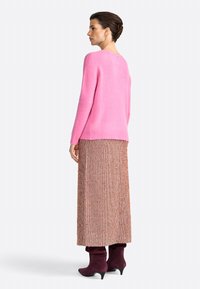 Maglione rosa brillante con scollo rotondo, abbinato a una lunga gonna a fantasia nei toni del marrone. Il modello indossa stivali con tacco viola.