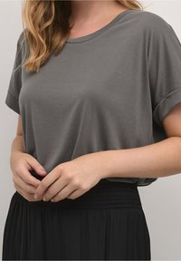 Grå kortärmad topp i ett mjukt material, avslappnad passform med rund halsringning, kombinerad med en svart plisserad kjol med resårmidja.