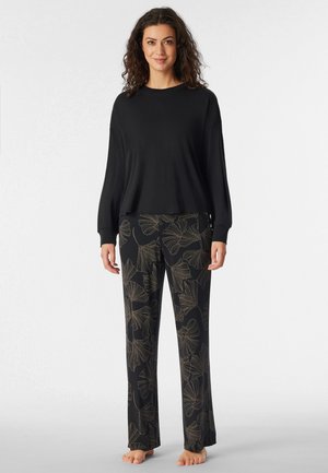 Schwarzes Langarmoberteil kombiniert mit schwarzen Hosen, die ein goldenes Blumenmuster aufweisen. Lockere Passform, weicher Stoff und weit geschnittenes Design.