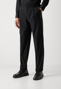 Black pleated trousers made of lightweight fabric, featuring side pockets and a tailored fit. Worn with black shoes and a dark shirt.