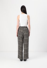 Pantalons à larges jambes à motif zèbre noir et beige avec une taille haute, associés à un débardeur ajusté blanc. Tissu lisse et coupe décontractée.