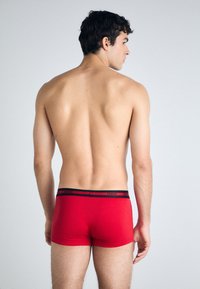 Røde boksershorts med en tettsittende passform og en svart merkevareliv. Stoffet ser glatt og elastisk ut, designet for komfort.