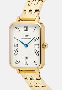Montre rectangulaire en acier inoxydable doré avec un cadran texturé blanc, des chiffres romains noirs, des aiguilles bleues et un affichage de la date en bas.