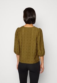 Blusa testurizzata verde oliva con maniche corte e puffate e scollatura rotonda. Presenta un motivo sottile di traforo e punti.