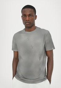 Grå kortærmet t-shirt lavet af glat stof med et diskret logo-mønster hele vejen rundt og rund halsudskæring.