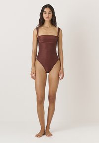 Brązowy jednoczęściowy strój kąpielowy z kwadratowym dekoltem, szerokimi ramiączkami i wysokim krojem nogawek. Gładka tekstura z subtelnym połyskiem.