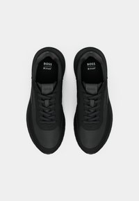 Chaussures de sport noires au design élégant, fabriquées en matériau synthétique lisse, avec lacets à l'avant et semelles intérieures rembourrées embossées du nom de la marque.