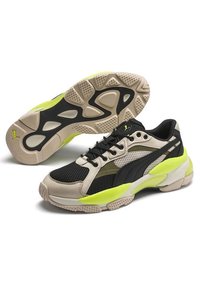 Masivní tenisky s kombinací černé síťoviny a béžových syntetických materiálů, s neonově zelenými akcenty, texturovanou podrážkou a výrazným brandingem.