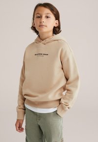 Béžová mikina vyrobená z mäkkého materiálu, s predným vreckom a kapucňou na šnúrku. Má potlač "BLUE RIDGE DENIM" a "STAY FEARLESS" v čiernej farbe.