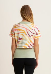 T-shirt cropped con stampa a zebre multicolore, con strisce gialle, rosa e viola, realizzato in tessuto morbido. Indossato sopra un top verde aderente.