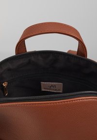 Borsa a tracolla in pelle marrone testurizzata con chiusura a zip e fodera in tessuto nero. Presenta una piccola tasca interna con zip e etichetta del marchio.