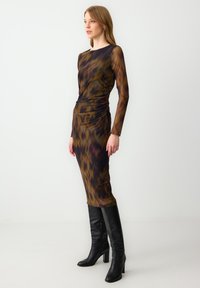Mouwe mouwen jurk in een veelkleurig, abstract patroon met een getailleerd ontwerp en geplooide details aan de zijkant, gecombineerd met zwarte kniehoge laarzen.