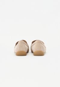 Beige mokasiner i semsket skinn med rund tupp og elastiske sideakkenter, med en lys brun gummisåle og glatt tekstur.