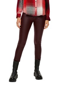 Pantalones slim-fit burdeos con una textura suave, combinados con una camisa de cuadros roja. Botines negros gruesos de tobillo completan el conjunto.