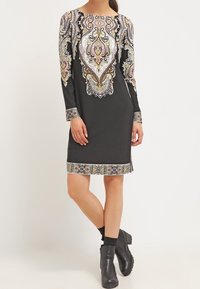 Robe noire à manches longues présentant des motifs cachemire complexes en blanc, or et orange sur les épaules et l'ourlet. Conçue avec une coupe droite.