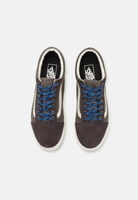 Baskets en daim marron avec des lacets bleus à motifs, accents blancs et semelle en caoutchouc ; elles présentent un col rembourré et un logo sur la languette.