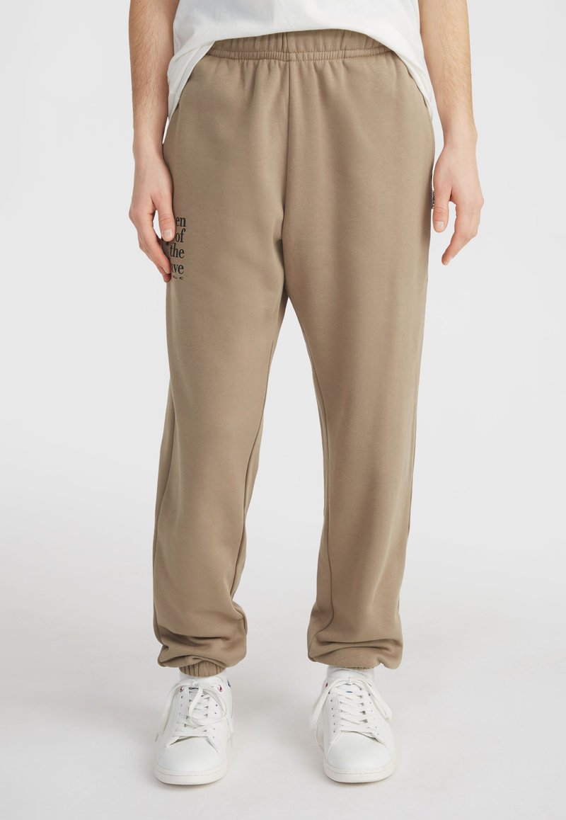 Beige sweatpants met een elastische tailleband en boorden, met een geprinte tekstdetail op de linkerdij en een gladde stoftextuur.
