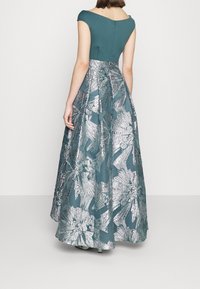 Robe de soirée teal à manches courtes, présentant un corsage ajusté et une jupe évasée ornée de motifs floraux argentés. Fermeture éclair au dos.