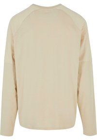 Beige hosszúujjú ing, laza szabással, raglán ujjakkal, kerek nyakkivágással és sima, puha szövet textúrával.