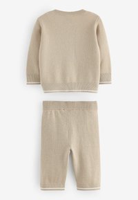 Ensemble tricoté beige en deux pièces comprenant un pull à manches longues et un short avec des finitions blanches au niveau des poignets et de la taille. Texture douce.
