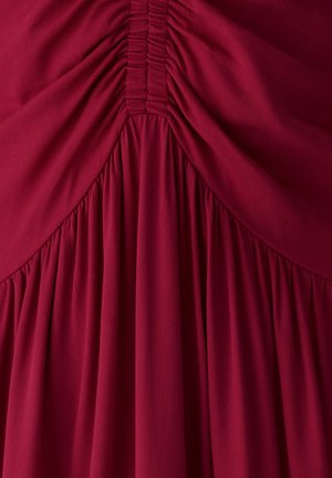 Dyb rød stof med gathered og ruched detaljer i midten, der skaber bløde lodrette folder og tekstur.