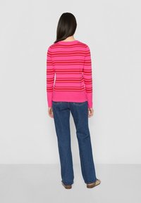 Pullover di un vivace rosa con strisce rosse orizzontali, maniche lunghe e scollatura tonda. Abbinato a pantaloni in denim azzurro a gamba larga.
