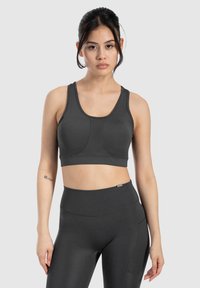 Sujetador deportivo gris oscuro con una tela suave y elástica. Presenta tirantes anchos y costuras para mayor soporte. Se lleva con leggings de cintura alta gris oscuro a juego.