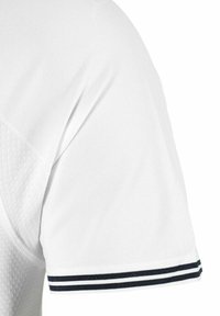 Camisa polo blanca con un tejido texturizado y un borde a rayas negras en el cuello y las mangas. Ajuste clásico, diseño limpio.