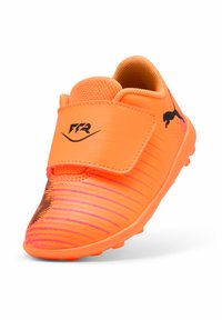 Scarpa da calcio sintetica arancione con corpo testurizzato, cinturino in velcro e accenti neri. Presenta un motivo a strisce e una suola in gomma stampata per la presa.