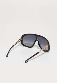Occhiali da sole neri con montatura oversize, lenti sfumate e aste accentate in oro con dettagli intagliati e punte delle aste nere eleganti.