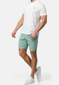 Weißes Baumwollpolohemd mit kurzen Ärmeln, grüne Denim-Shorts und weiße Turnschuhe. Mit gesticktem Logo auf der Brust, einfarbiges Design.