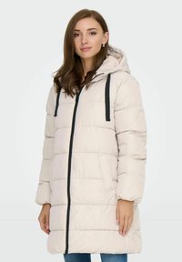 Helles beiges Puffer-Jacke mit Kapuze, ausgestattet mit einem Frontreißverschluss, schwarzen Akzenten und zwei Seitentaschen. Der Stoff wirkt glatt und gesteppt.