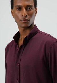 Bordeauxrode overhemd met knopen, voorzien van een spitse kraag en een subtiele textuur. Heeft knopen aan de voorkant en een glad, aansluitend ontwerp.