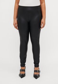 Fekete műbőr leggings, sima textúrával, karcsú fazonnal és magas derékkal. Fekete, csatos, hegyes orrú magassarkú cipővel párosítva.