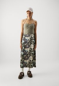 Grön ribbade bustier topp ihop med en lång mönstrad kjol i marinblått, vitt och mint; bruna kraftiga skor; beige keps; hoopörhängen.