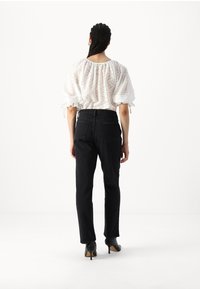Mustmustest püksid kõrge vöökohaga ja sirge säärega, millele on sobitatud valge tekstuuriga puff-sleevesi ja kogutud kaelusega blouse.