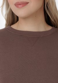 Hnedý rebrovaný sveter so širokým výstrihom a jemným detailom V-švu. Mäkka textúra, priliehavý strih.