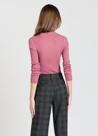 Figurbetonter, gerippter rosa Oberteil mit langen Ärmeln, kombiniert mit hoch taillierten karierter Hose in Schwarz und Weiß. Weicher Stoff und maßgeschneiderter Schnitt.