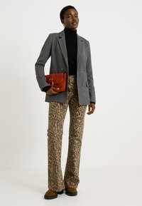 Blazer gris à double boutonnage porté sur un col roulé noir, associé à un pantalon évasé à imprimé léopard. Tenant une pochette rouge avec une boucle dorée.
