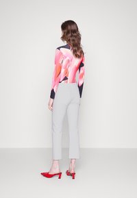 Pitkähihaista puseroa, jossa on vaaleanpunainen kukkakuosi, on yhdistetty vaaleanharmaisiin cropped-housuihin ja punaisiin korkokenkiin. Pehmeä materiaali ja moderni siluetti.