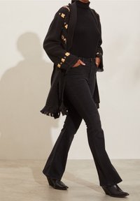 Black knitted cardigan with floral embroidery, paired with ribbed black turtleneck and dark flared jeans. Heeled black boots complete the look.