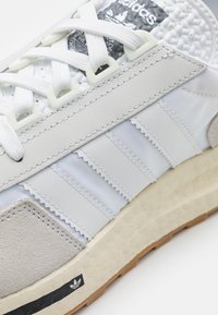 Vit sneakers med texturerad mesh- och slät läderöverdel, med grå mockadetaljer och beige gummisula. Tredelad design.