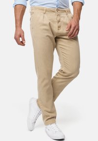 Beige puuvillasekoitekankaat, suoralla mitoituksella, etupleat, sivutaskut ja nappikiinnitys. Yhdistetty valkoisiin lenkkareihin.