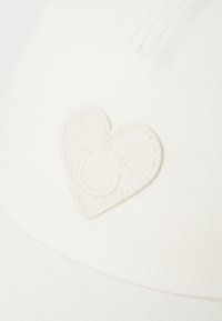 White baseball cap made of textured fabric featuring an embroidered heart logo in a matching color on the front.