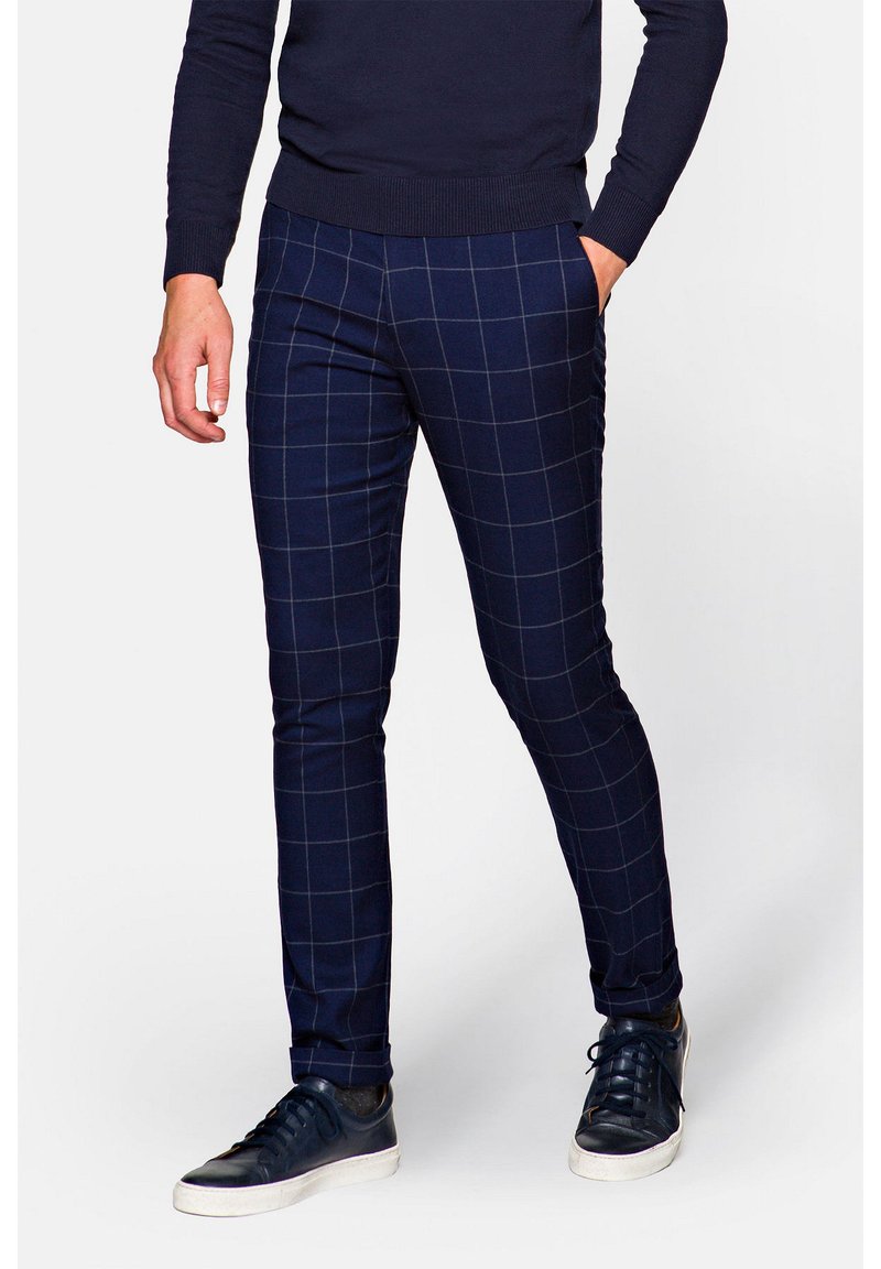 Granatowe spodnie w kratę wykonane z tkaniny o gładkiej teksturze, o dopasowanym kroju i bocznych kieszeniach, zestawione z ciemnymi sneakersami.