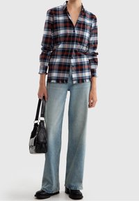 Rutigt skjorta i blått, röd och vitt, med knäppning fram och fransad nederkant, parat med ljusblå vida jeans och en svart handväska.